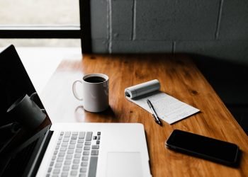 A picture of a cup of coffee on a desk with a computer and a notepad ready to make a change management plan.