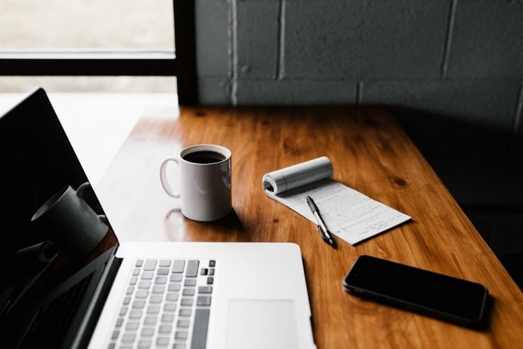 A picture of a cup of coffee on a desk with a computer and a notepad ready to make a change management plan.